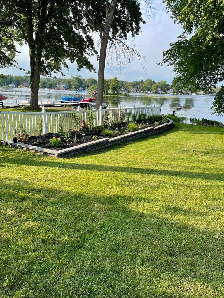 Newly installed mulch garden bed with fresh plantings along a lakefront fence line